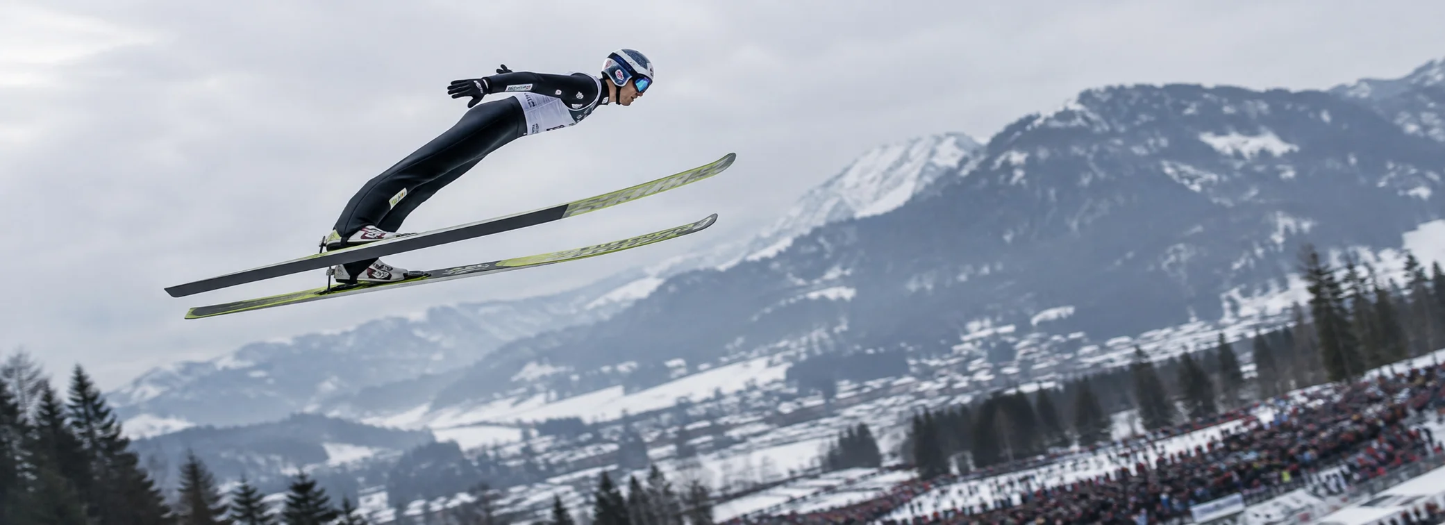 Olympic ski jumper soaring in full flight over winter alpine mountains during kinematic aerodynamic and biomechanical load analysis.